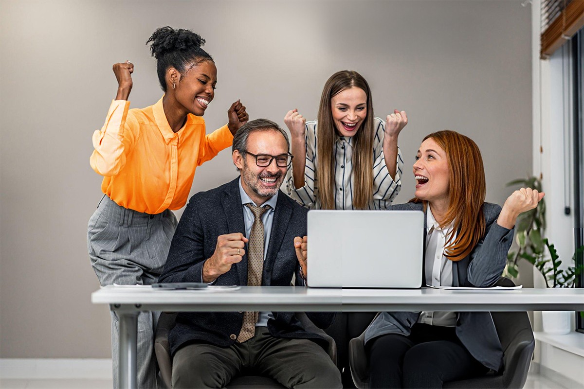 4 people looking at a laptop screen showing excitement